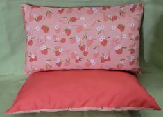 a pink pillow sitting on top of a bed next to a red pillow cover with white flowers