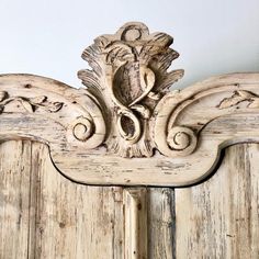 an old white wooden headboard with carvings on the top and bottom panel, in front of a wall