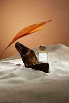 a bottle of perfume sitting on top of a bed next to an orange flower and a leaf