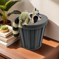 a toy racoon sitting in a trash can on top of a wooden table