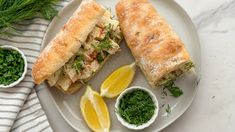 a white plate topped with a cut in half sandwich next to lemon wedges and parsley