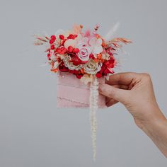 a person holding a flower bouquet in their left hand, on a gray background with white and red flowers