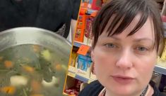 a woman standing in front of a pan filled with food and looking at the camera