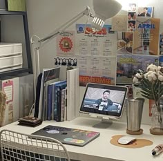 a desk with a computer monitor, keyboard and flowers in a vase next to it