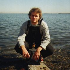 a man sitting on top of a rock next to the ocean with his feet in the water