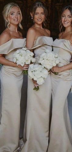 three bridesmaids pose for a photo in their wedding gowns and bouquets