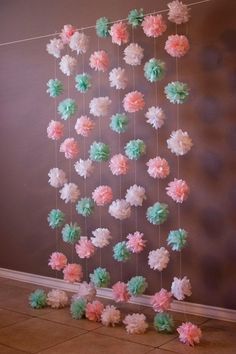 some pink and green flowers hanging from a string on the wall in front of a brown wall