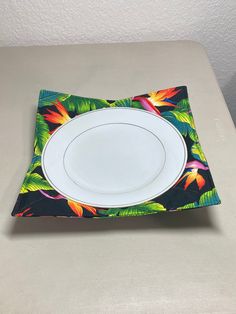 an empty plate on top of a placemat with colorful flowers and green leaves in the center