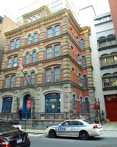 a police car parked in front of a tall building on a city street with cars passing by