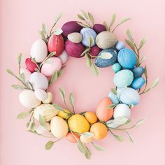 an easter wreath made out of colored eggs and leaves on a pink background with the words happy easter written below it