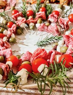 an arrangement of meats and vegetables arranged on a platter with olives, tomatoes, and rosemary