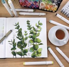 an open book on a table with markers, pens and watercolors next to it