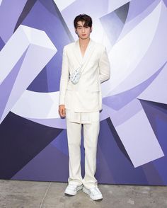 a man in a white suit and sneakers standing on a cement floor next to a purple wall