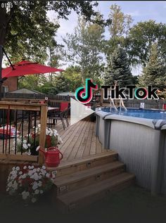 an above ground swimming pool with decking and umbrellas in the background, surrounded by flowers