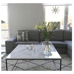 a living room with a couch, coffee table and vase on the floor in front of a large window