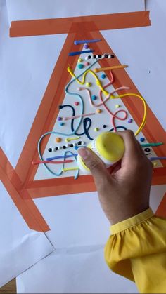 a child's hand holding an object in front of a christmas tree made out of construction paper