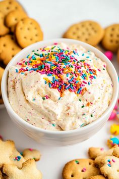 a bowl filled with white frosting surrounded by cookies and sprinkles