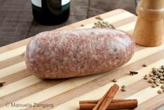 a large sausage sitting on top of a wooden cutting board next to spices and wine bottles