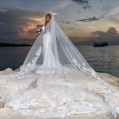 the bride is standing on rocks by the water with her veil blowing in the wind