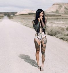 a woman walking down a dirt road talking on a cell phone with tattoos on her body