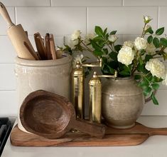 kitchen utensils and wooden spoons sit on a cutting board next to flowers