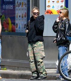 two women are standing on the sidewalk talking to each other and one is holding a cell phone