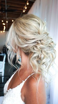 a woman with blonde hair in a wedding dress looking down at her shoulder length hairstyle