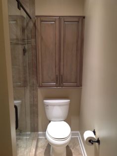 a white toilet sitting inside of a bathroom next to a walk in shower and wooden cabinets