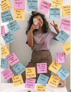 a woman sitting on top of a toilet covered in post it notes and holding a cup