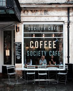 two people sitting at a table in front of a coffee shop