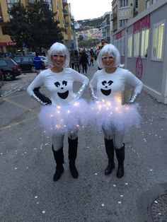 two women dressed up in costumes standing on the side walk with lights all around them