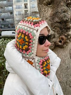 a woman wearing sunglasses and a crocheted hat is standing next to a tree