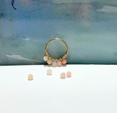 three different colored stones sitting on top of a white surface next to a gold ring