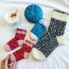 someone is knitting socks and yarn next to a cup of coffee on a white bed