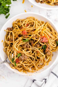 two white bowls filled with spaghetti and meat on top of a marble table next to parsley