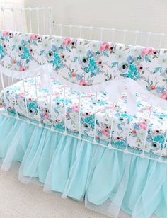 a baby crib with blue ruffled bedding and pink flowers on the cover