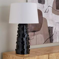 a black table lamp sitting on top of a wooden dresser next to a wall painting