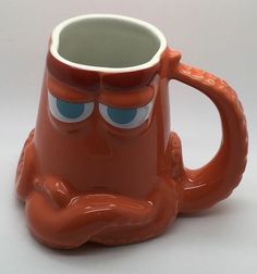 an orange coffee mug with eyes and hands on it's face, sitting in front of a white background