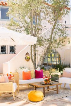 an outdoor living area with white furniture and colorful pillows on the couches, coffee table, and umbrella