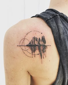 the back of a woman's shoulder with mountains and trees tattoo on her left arm