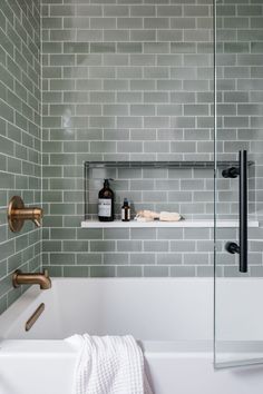 a white bath tub sitting next to a shower with green tile on the walls and floor