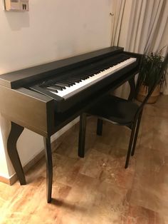 a black piano sitting in front of a window next to a chair and potted plant