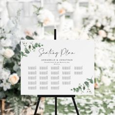 a white sign with greenery and flowers on it in front of a floral backdrop