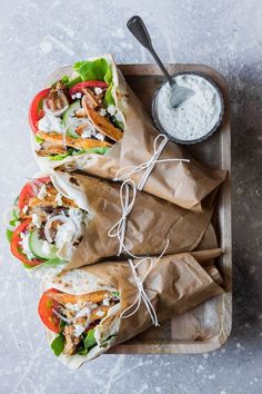 three pita sandwiches with lettuce, tomatoes and other toppings on a tray