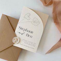 a wedding card with a ring on it next to an envelope and a ribbon tied around it