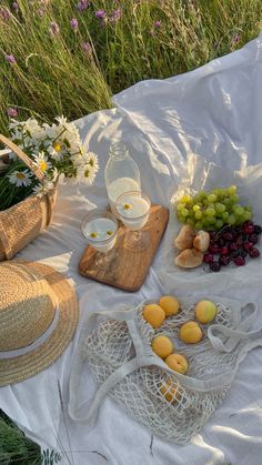 the table is covered with white cloths and fresh fruit, including grapes, oranges, lemons, straw hats, and wine glasses