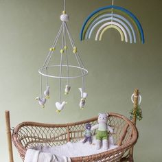 a wicker crib with two teddy bears and a rainbow mobile hanging from the ceiling