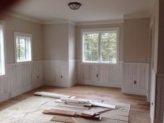 an empty room with wood flooring and white paneling on the walls, windows in the corner