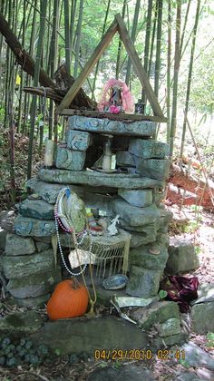 an outdoor fireplace made out of rocks in the woods with a pumpkin sitting on it