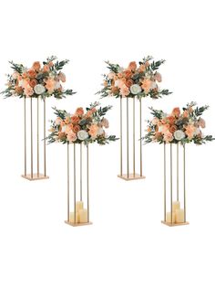 four tall gold vases with flowers and candles on stands in front of a white background